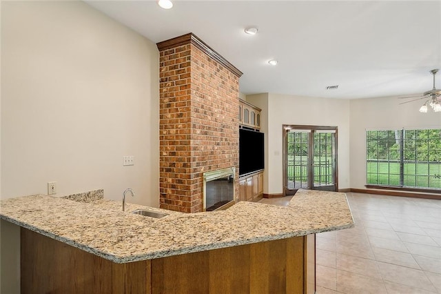 kitchen with sink, light stone counters, kitchen peninsula, light tile patterned floors, and a brick fireplace