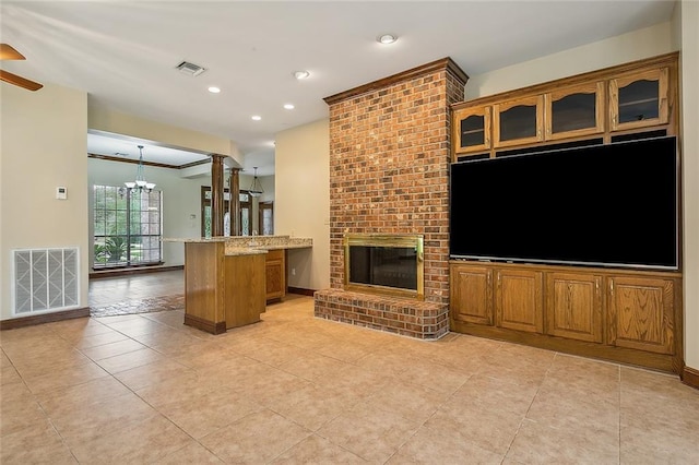 unfurnished living room featuring decorative columns, ceiling fan with notable chandelier, light tile patterned flooring, and a fireplace