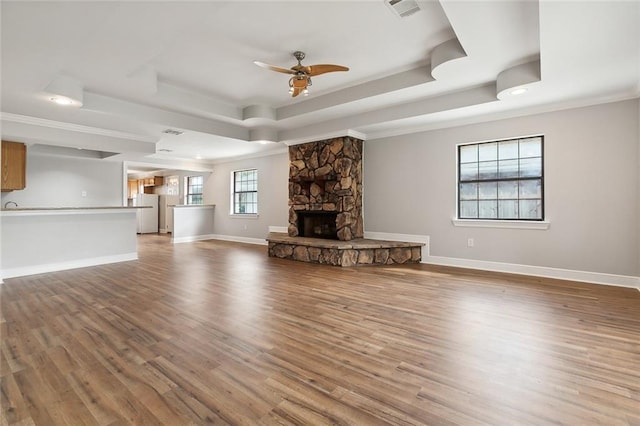 unfurnished living room featuring a stone fireplace, hardwood / wood-style flooring, ceiling fan, and a tray ceiling