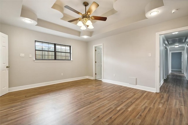 spare room with ceiling fan, a raised ceiling, and dark hardwood / wood-style flooring