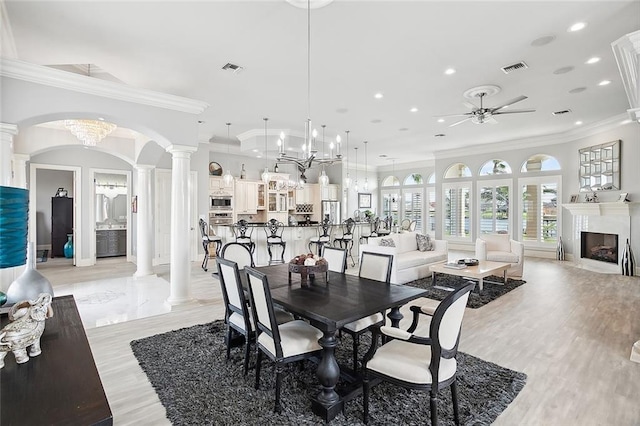 dining space with ceiling fan with notable chandelier, crown molding, light hardwood / wood-style flooring, and ornate columns