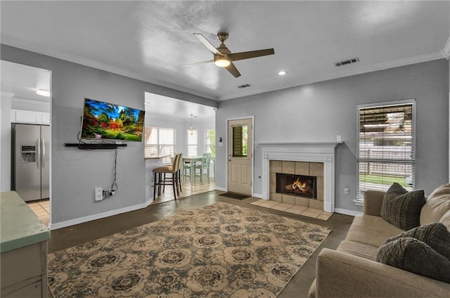 living room featuring ceiling fan, plenty of natural light, a tile fireplace, and ornamental molding