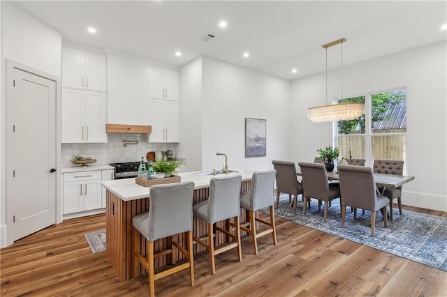 kitchen with light hardwood / wood-style flooring, backsplash, decorative light fixtures, a kitchen island with sink, and white cabinets