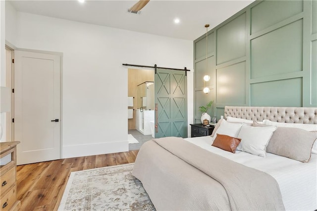 bedroom with connected bathroom, a barn door, ceiling fan, and hardwood / wood-style floors