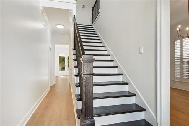 stairs featuring a wealth of natural light, wood-type flooring, and a notable chandelier