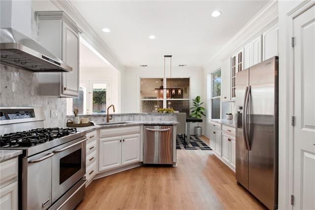 kitchen featuring wall chimney range hood, white cabinets, sink, and stainless steel appliances