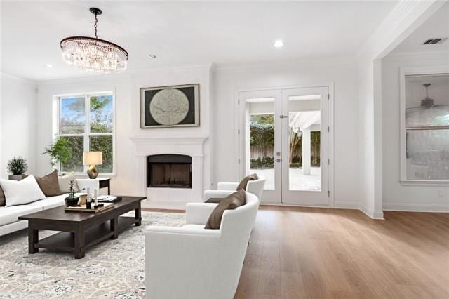 living room featuring light hardwood / wood-style floors, a healthy amount of sunlight, an inviting chandelier, and ornamental molding