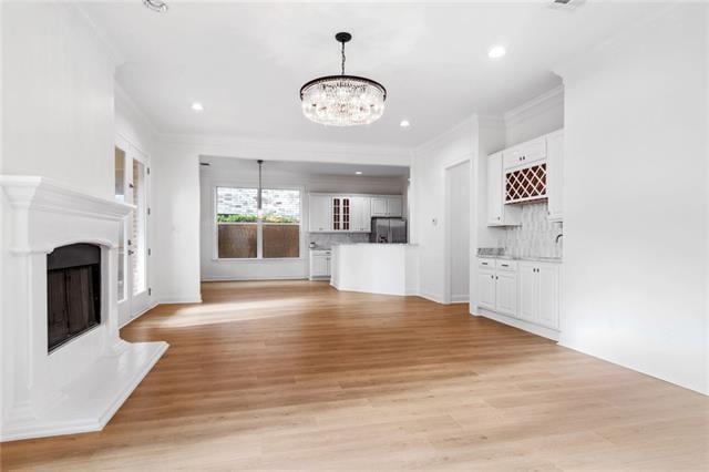 unfurnished living room featuring a notable chandelier, light hardwood / wood-style floors, and crown molding