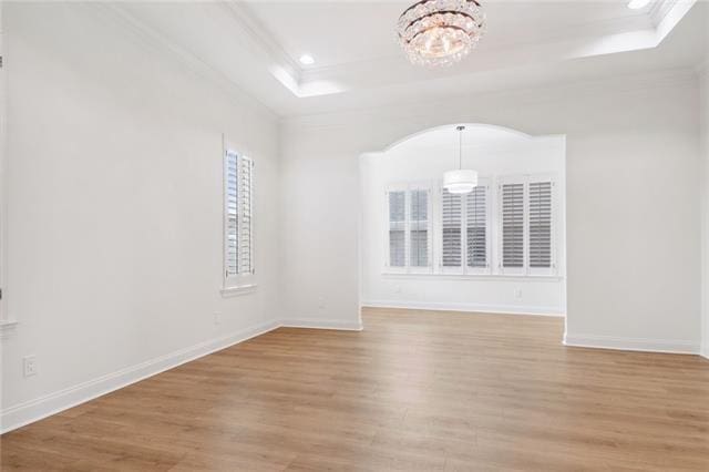 unfurnished room with ornamental molding, light hardwood / wood-style floors, a chandelier, and a tray ceiling