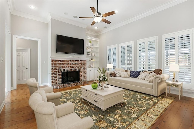 living room featuring crown molding, ceiling fan, wood-type flooring, and a brick fireplace