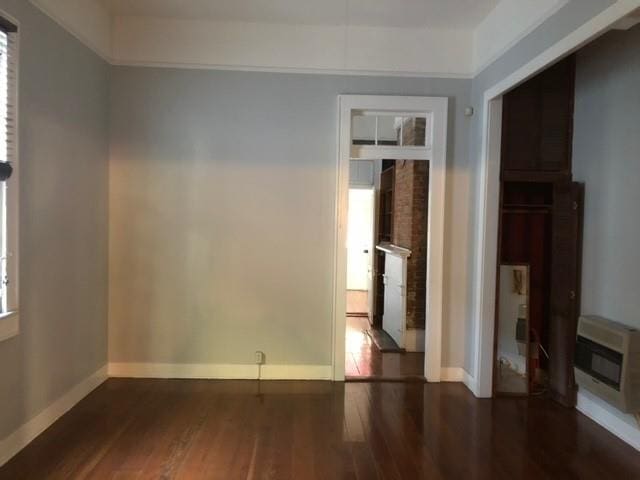 empty room with dark hardwood / wood-style flooring, heating unit, and a healthy amount of sunlight