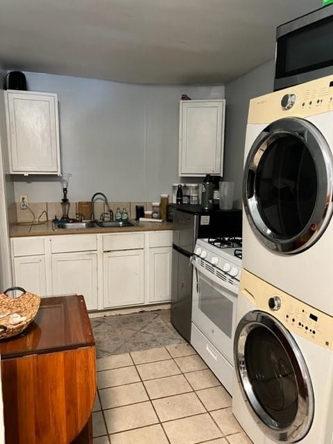 928 Independence St, New Orleans, LA 70117 - kitchen with white gas range, light tile patterned floors, stacked washing maching and dryer, a sink, and stainless steel microwave