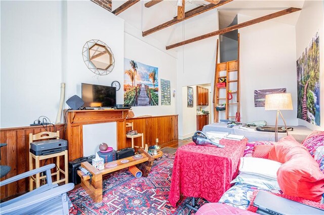 living room featuring beamed ceiling, high vaulted ceiling, ceiling fan, and wood walls