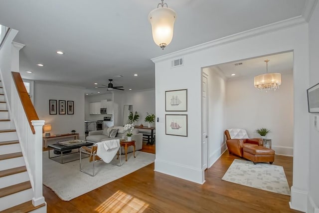 living room featuring wood-type flooring, crown molding, and ceiling fan with notable chandelier