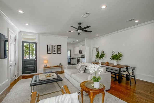 living room with dark wood-type flooring, ceiling fan, and crown molding