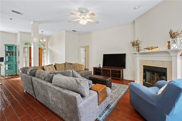 living room featuring dark hardwood / wood-style floors, a tile fireplace, ceiling fan with notable chandelier, and crown molding