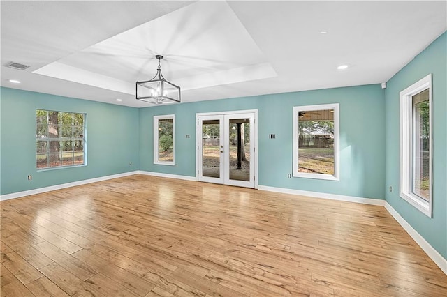 interior space featuring a raised ceiling, light wood-type flooring, french doors, and a notable chandelier