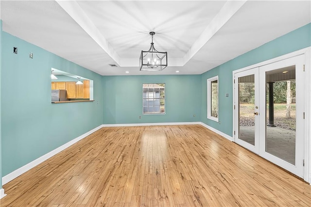 unfurnished dining area with a tray ceiling, light wood-style floors, french doors, and baseboards