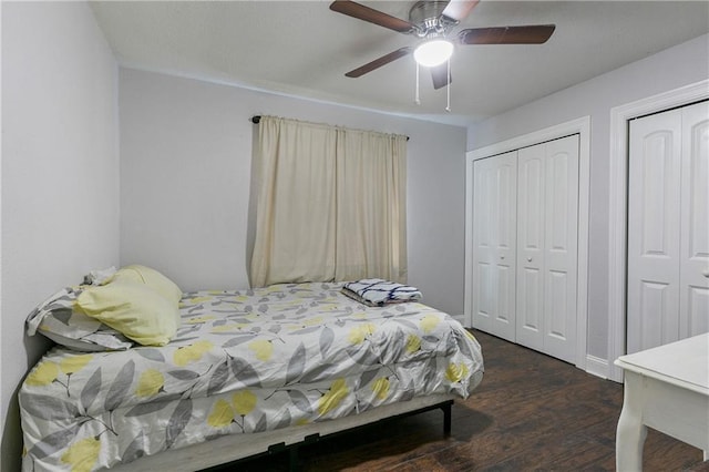 bedroom with dark wood-type flooring, ceiling fan, and two closets