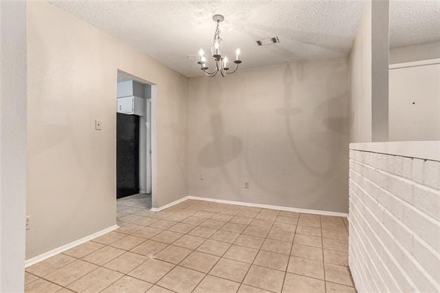 unfurnished room featuring a chandelier, light tile patterned floors, and a textured ceiling