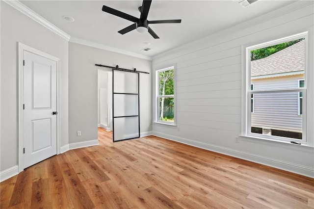 unfurnished bedroom featuring ceiling fan, ornamental molding, a barn door, and light hardwood / wood-style flooring