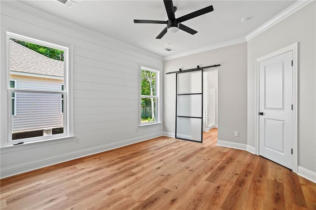 unfurnished bedroom featuring crown molding, a barn door, ceiling fan, and light wood-type flooring