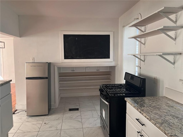 3633 Franklin Ave, New Orleans, LA 70122 - kitchen featuring range with gas stovetop, freestanding refrigerator, light marble finish floors, dark stone countertops, and white cabinetry