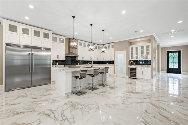 kitchen featuring recessed lighting, beverage cooler, stainless steel built in fridge, a kitchen bar, and backsplash