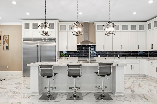 kitchen with wall chimney range hood, built in refrigerator, marble finish floor, and recessed lighting