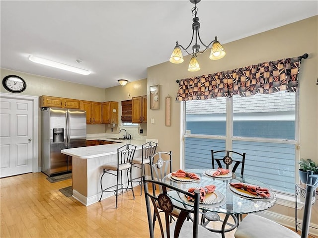 kitchen featuring light hardwood / wood-style floors, sink, kitchen peninsula, stainless steel refrigerator with ice dispenser, and hanging light fixtures