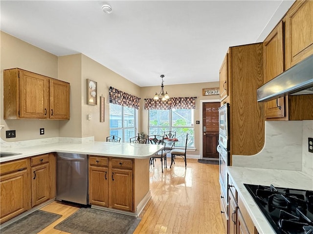 kitchen featuring stainless steel appliances, light hardwood / wood-style floors, kitchen peninsula, hanging light fixtures, and a chandelier