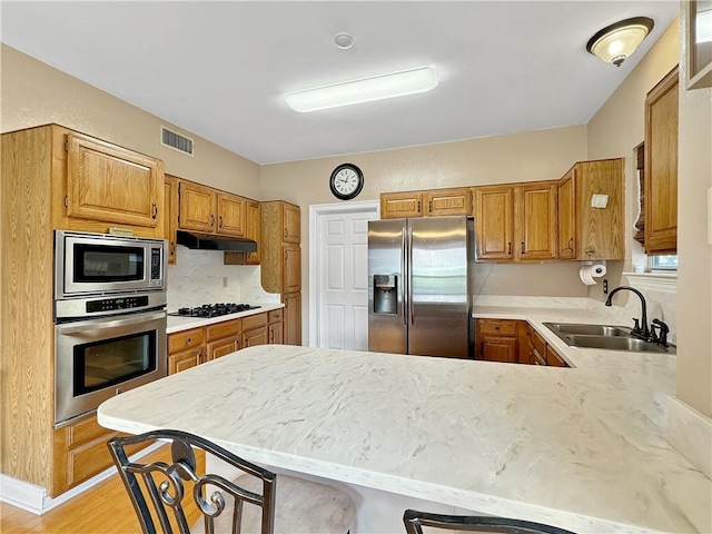 kitchen featuring stainless steel fridge with ice dispenser, gas cooktop, sink, a breakfast bar area, and kitchen peninsula