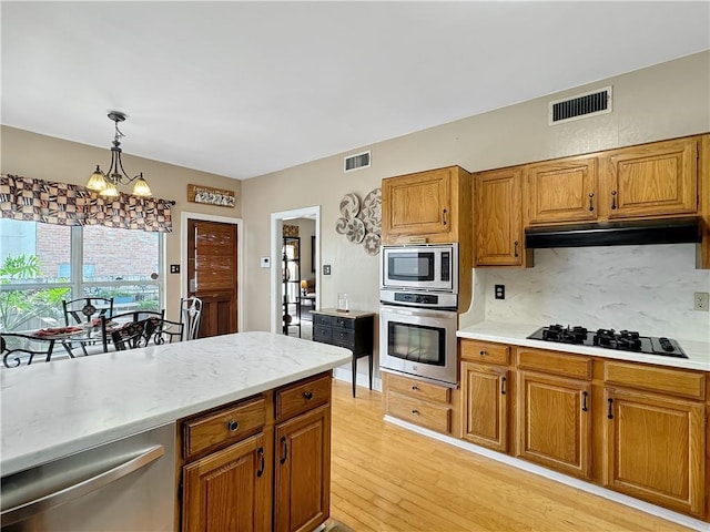 kitchen featuring tasteful backsplash, appliances with stainless steel finishes, hanging light fixtures, an inviting chandelier, and light hardwood / wood-style flooring