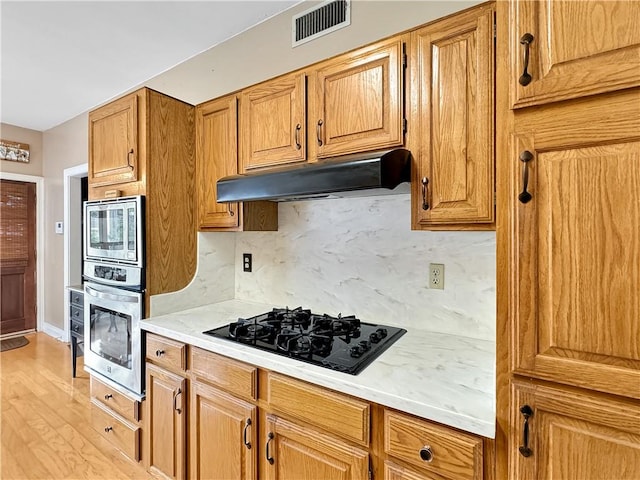 kitchen with light wood-type flooring, stainless steel appliances, and backsplash