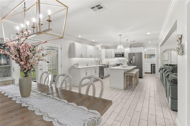 dining space featuring an inviting chandelier, sink, light hardwood / wood-style flooring, and crown molding