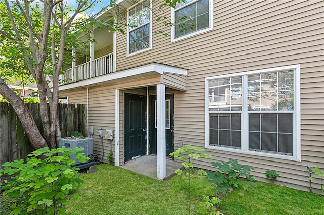 entrance to property with cooling unit, a lawn, and a balcony