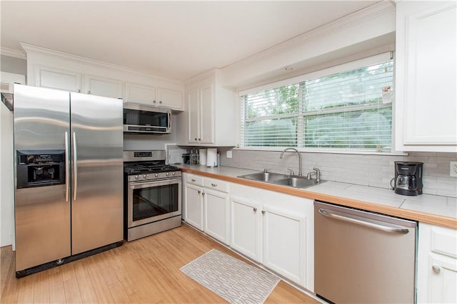 kitchen featuring stainless steel appliances, sink, tile counters, light hardwood / wood-style floors, and white cabinets