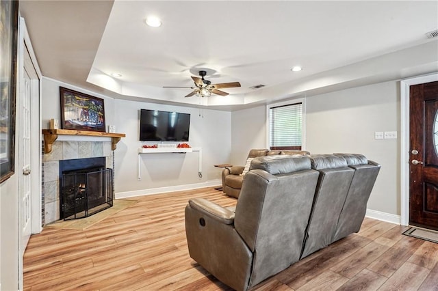 living room featuring baseboards, visible vents, light wood-style flooring, a tiled fireplace, and a raised ceiling