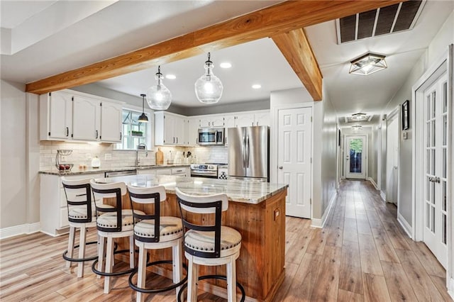 kitchen featuring appliances with stainless steel finishes, light wood-type flooring, beamed ceiling, white cabinets, and a center island