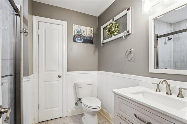 bathroom featuring a wainscoted wall, toilet, vanity, and a tile shower