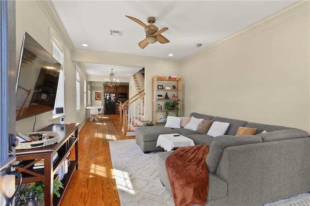 living room featuring wood-type flooring, ornamental molding, and ceiling fan with notable chandelier