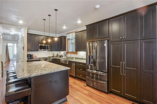 kitchen with stainless steel appliances, ornamental molding, a kitchen island, pendant lighting, and light wood-type flooring