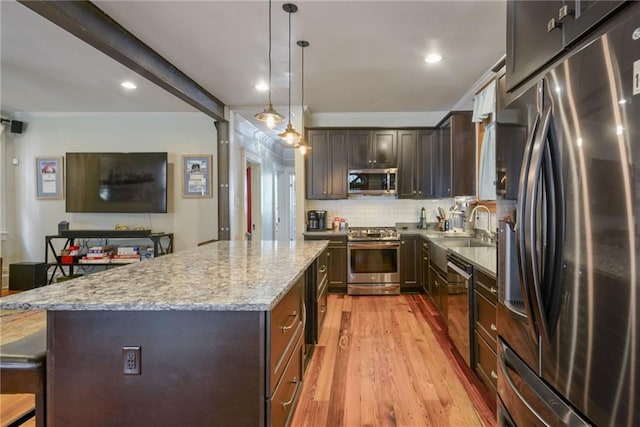 kitchen with appliances with stainless steel finishes, light stone countertops, hanging light fixtures, light hardwood / wood-style floors, and a center island