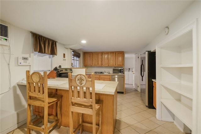 kitchen featuring stainless steel appliances, light tile patterned floors, a breakfast bar, and kitchen peninsula