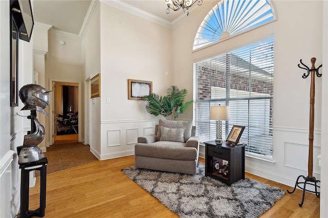 sitting room with a towering ceiling, wood-type flooring, a notable chandelier, and ornamental molding