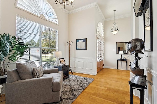 sitting room featuring a towering ceiling, light wood-type flooring, and ornamental molding