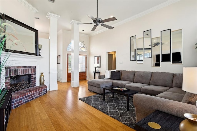 living room with hardwood / wood-style floors, a high ceiling, crown molding, a fireplace, and decorative columns