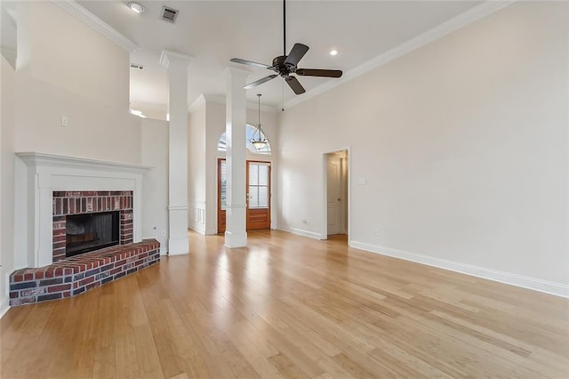 unfurnished living room featuring ceiling fan, a brick fireplace, a towering ceiling, light wood-type flooring, and ornamental molding