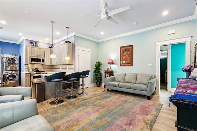 living room with stacked washer / drying machine, light wood-type flooring, ornamental molding, and ceiling fan