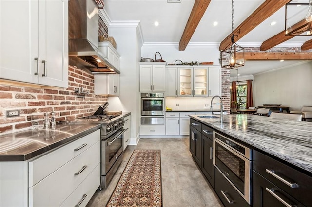 kitchen with white cabinetry, wall chimney range hood, appliances with stainless steel finishes, and decorative light fixtures